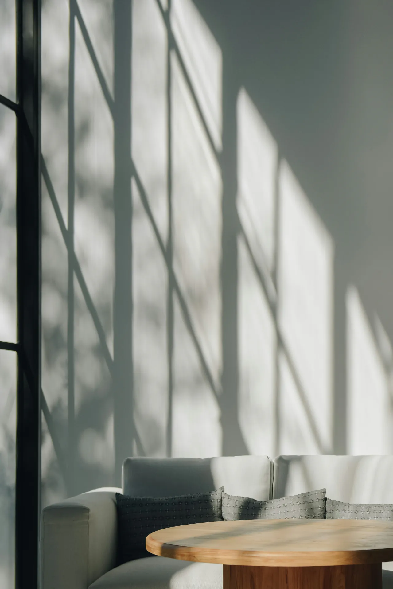 Window light falling across a gray wall above a sofa and a round table