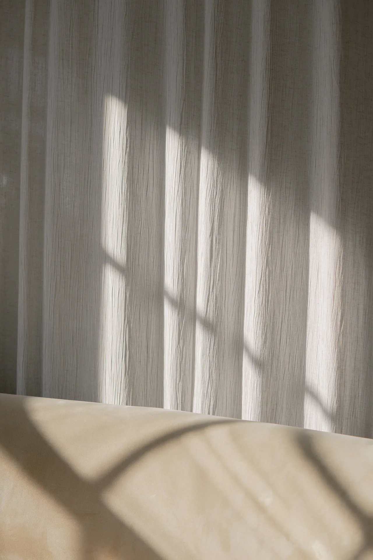 Sunlight through sheer curtains, its shadows across a plaster ledge