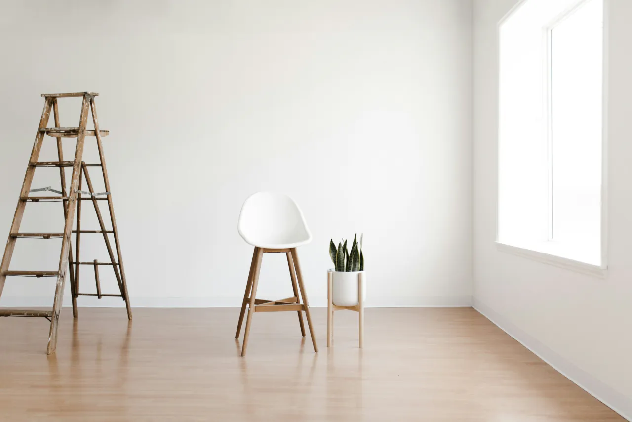 A wooden ladder, a white stool and a plant in an empty white room