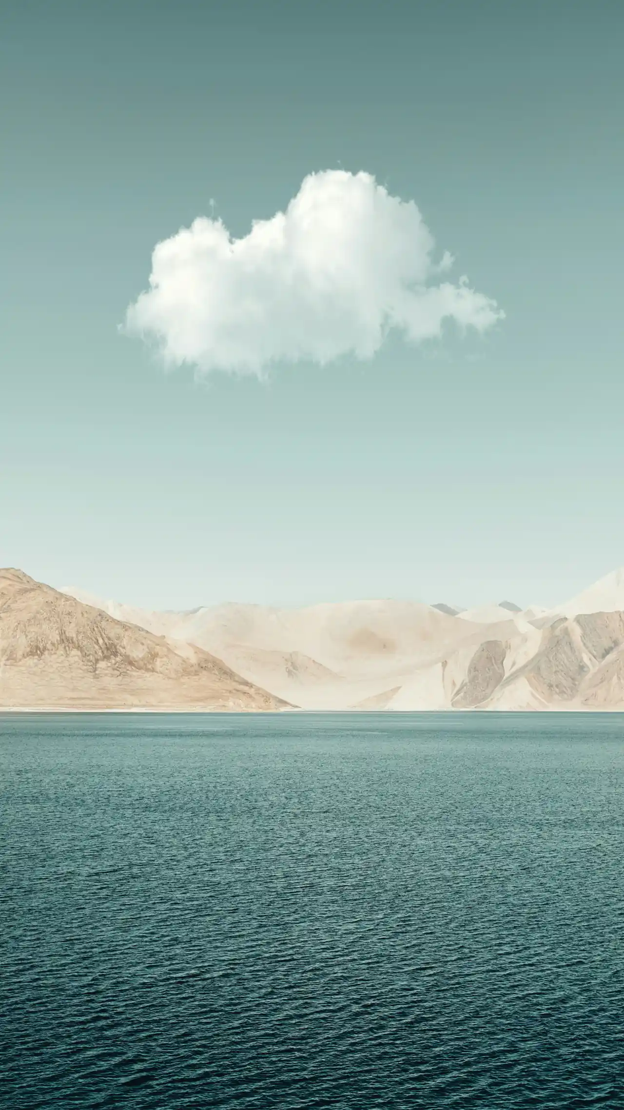 A single cloud over still green water and pale mountains