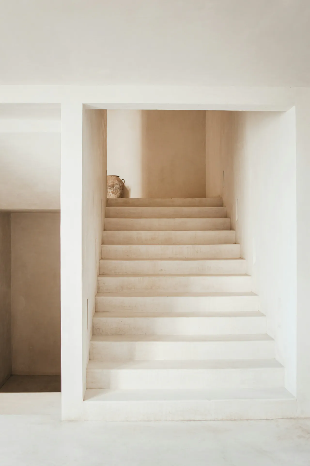 A white stair rising between plaster walls to a landing with a vase