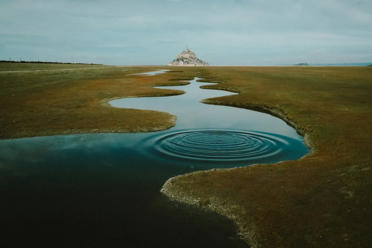A winding stream across a green marsh toward a distant island