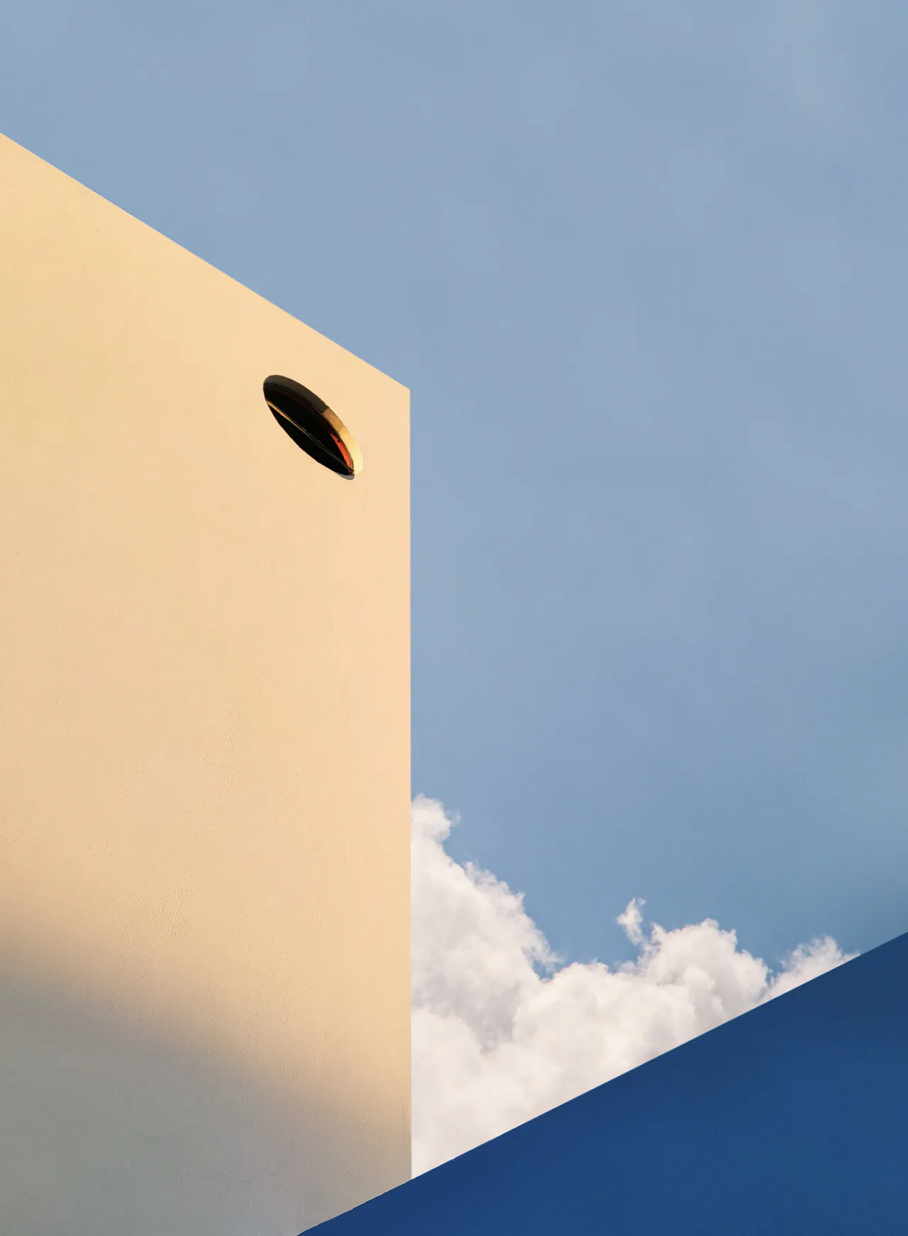A round window high in a sunlit wall, with a cloud behind it